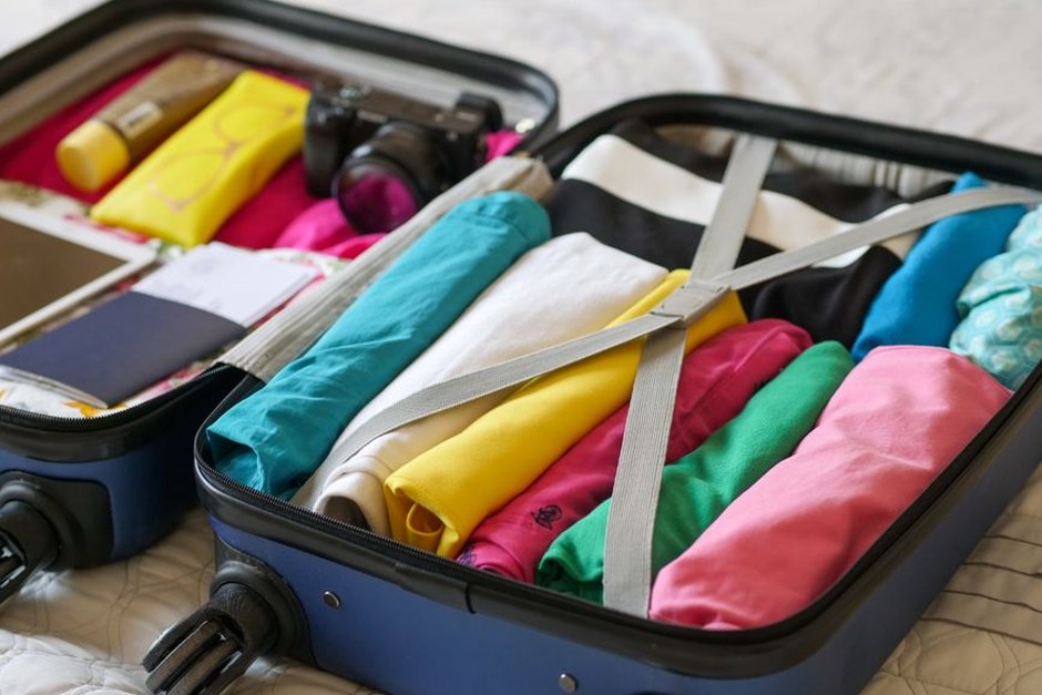 Open suitcase packed with folded clothes, a camera, and travel essentials.